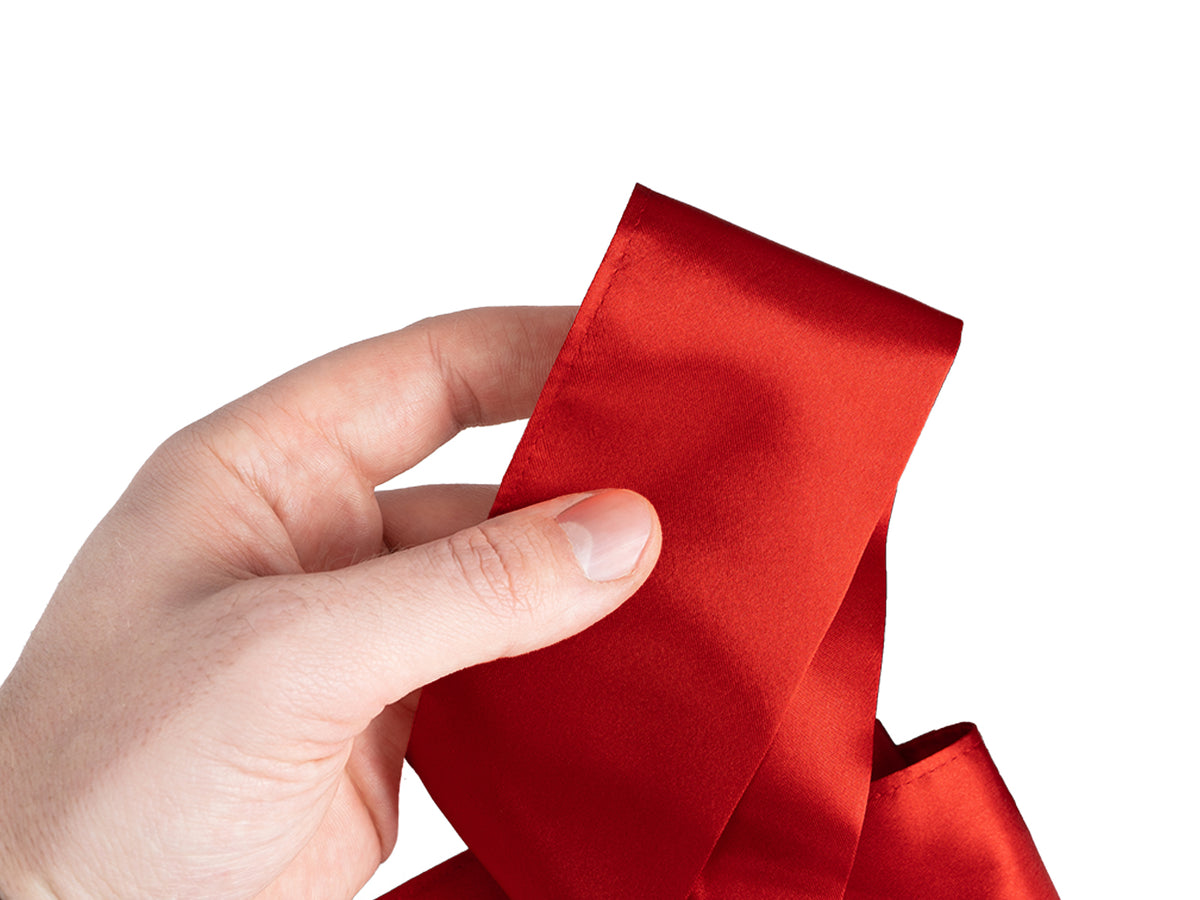 Augenbinde aus Glanzsatin in karmin-rot in der Hand – glatter, glänzender Satin