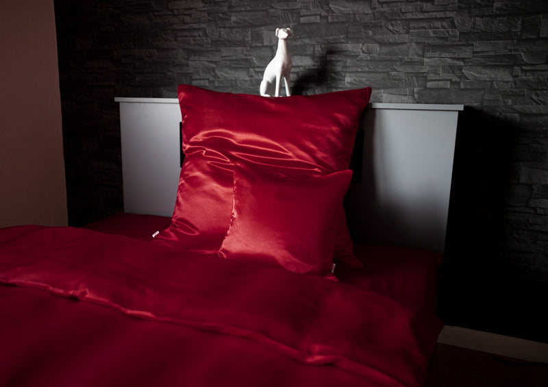Rote Glanz Satin Bettwaesche in einem schwarzen Bett.