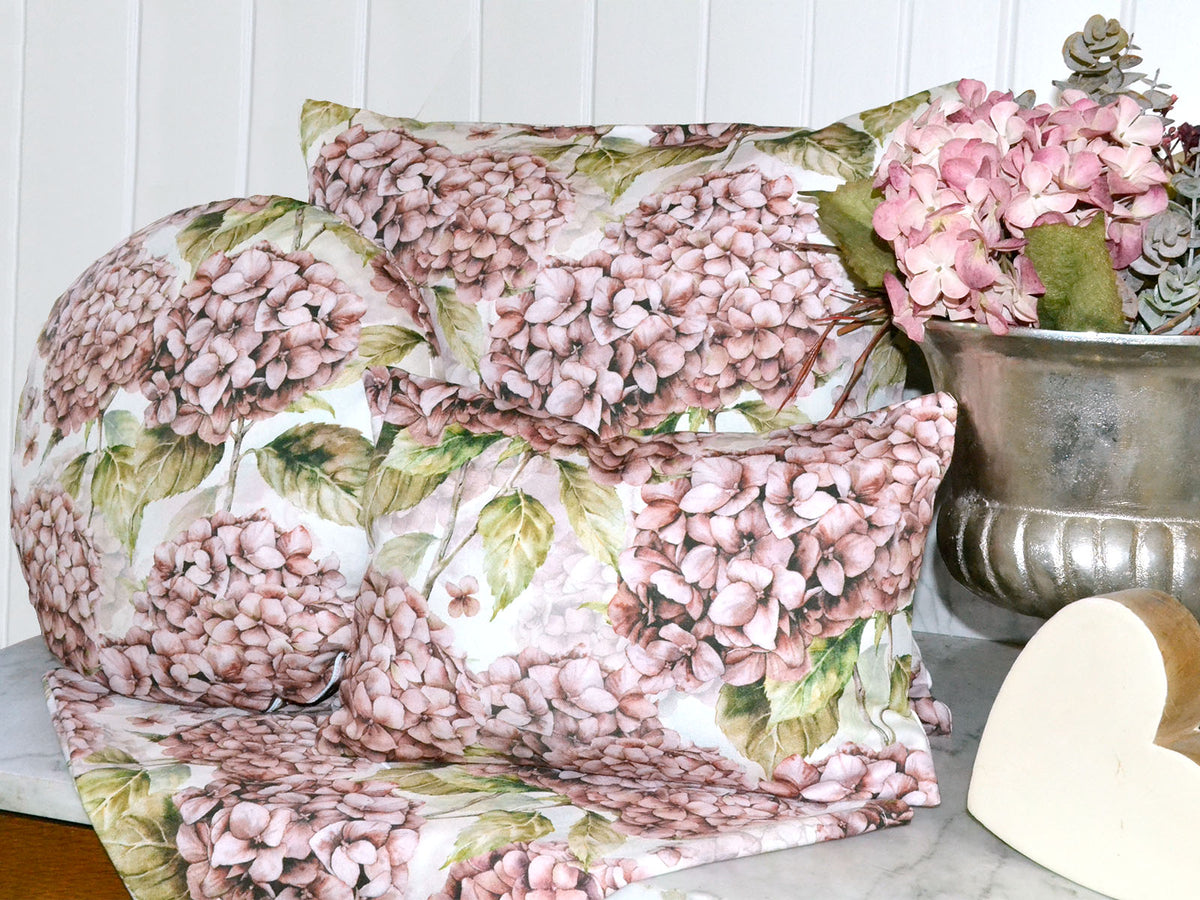 Drei Kissen bezogen mit je einem Kissenbezug im Landhausstil, bedruckt mit rosa/pinken Hortensien. Dekoriert auf einer Marmorplatte.